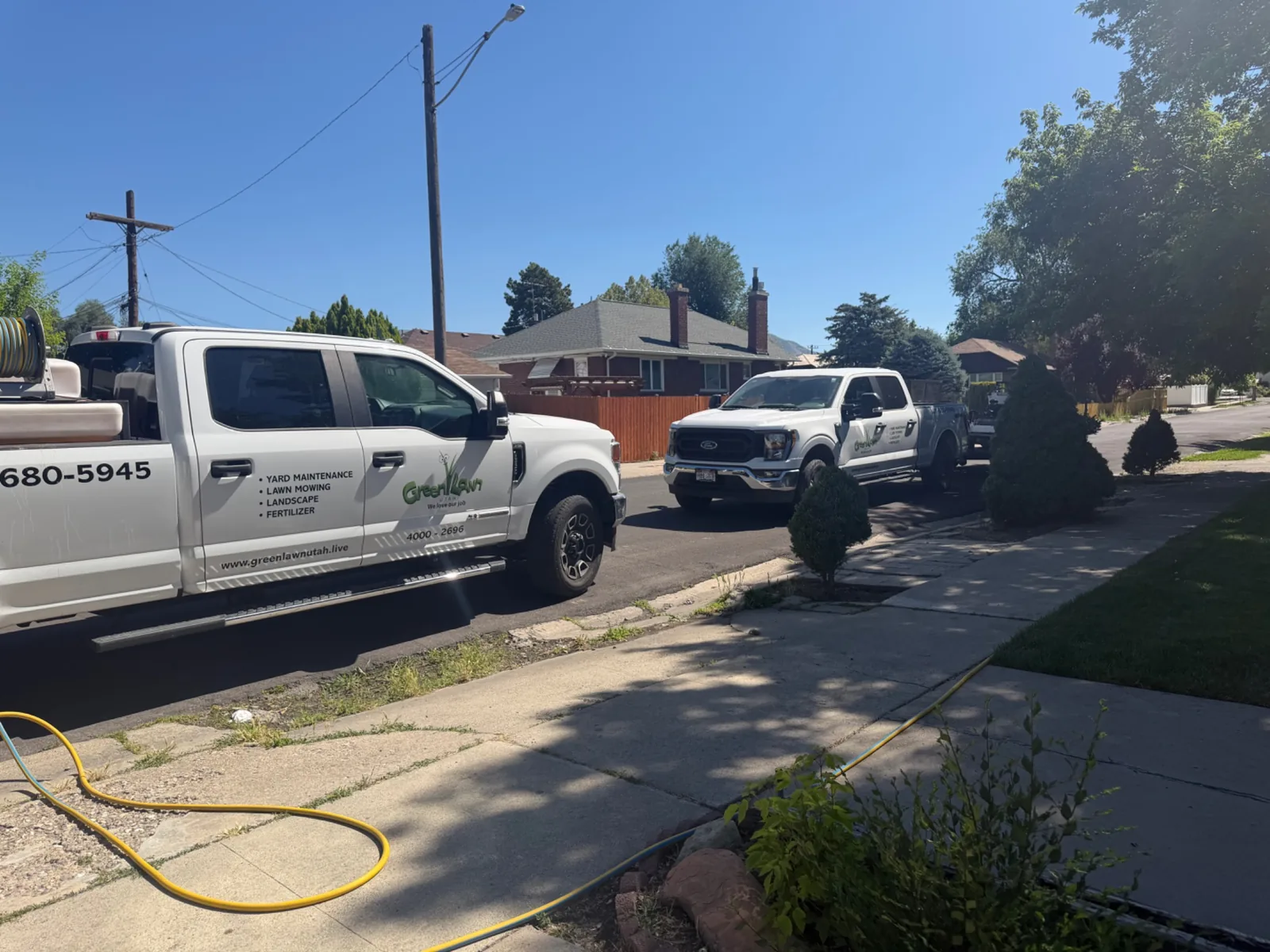 Two branded Green Lawn trucks parked on a Salt Lake Valley street during a job
